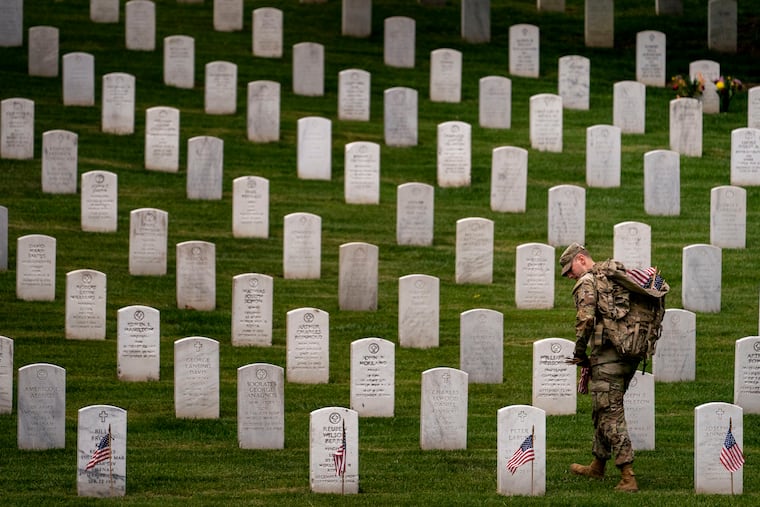 A member of the 3rd U.S. Infantry Regiment, also known as the Old Guard, places flags in front of each headstone for "Flags-In" at Arlington National Cemetery in Arlington, Va., to honor the nation's fallen military heroes ahead of Memorial Day 2023.