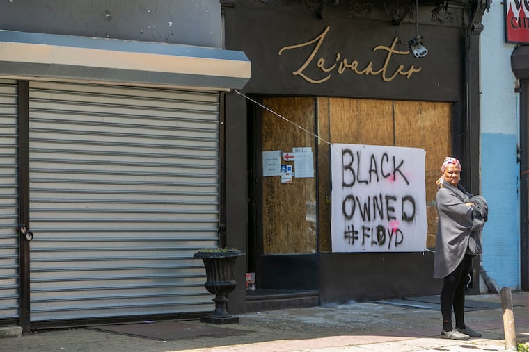 Stephanie Scurry stands in front of La'Vanter, a small boutique clothing store belonging to her son and daughter, on June 1, 2020. The windows had been boarded up from inside after they shut down during COVID-19, but a sign, "Black Owned #Floyd," spared it from looting.