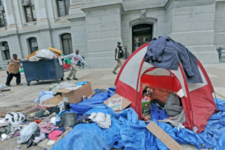 While Alicia Keen of Occupy Philadelphia rests inside her tent at Dilworth Plaza, sanitation crews haul out debris. (April Saul / Staff Photographer)