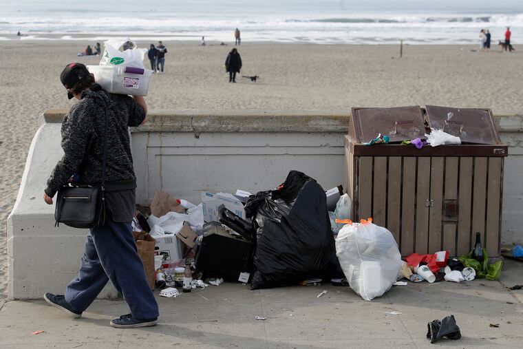 A woman walks past trash piled next to a garbage bin at Ocean Beach in San Francisco, Thursday, Jan. 3, 2019. Nonprofits, businesses and state governments across the country are paying bills and putting in volunteer hours in an uphill battle to keep national parks safe and clean for visitors as the partial U.S. government shutdown lingers. (AP Photo/Jeff Chiu)