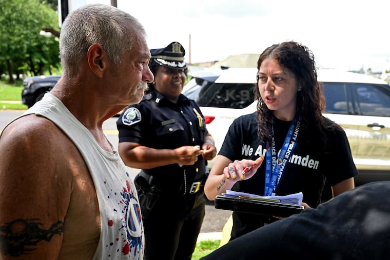 Center for Family Services lead counselor Lyzza Tyson (right) works with Camden County Metro Police Capt. Vivian Coley (rear) as she talks with Mike (no last name), who is living in the park at Waterfront South Raingardens, Wednesday, July 16, 2025. Some of the department’s new social workers are stationed inside the downtown police headquarters for walk-ins, while others are deployed in the field alongside officers doing door knocks, engaging transients at encampments, and making referrals for social services.