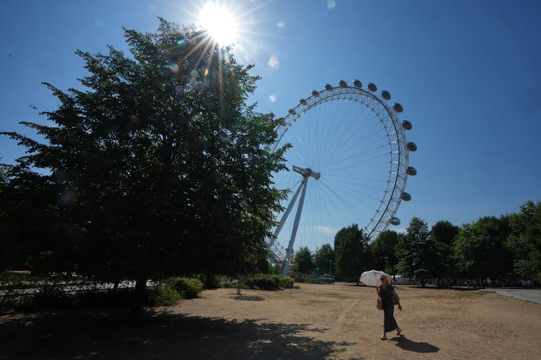 A woman shades under an umbrella as she walks past the London Eye during the fifth heatwave of the year in London, Thursday, Aug. 13, 2026. The extreme heat has caused an unusual amount of subsidence of houses in London.