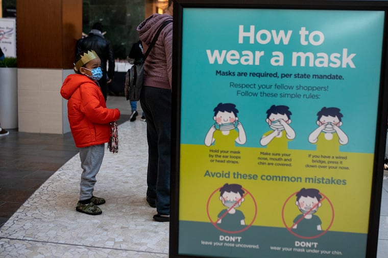 A child wearing a crown and mask waits next to his parent at Cherry Hill Mall on Saturday, Jan. 23.