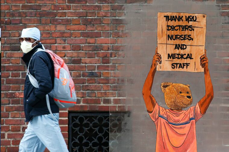 A pedestrian walks past a painting thanking doctors, nurses, and medical staff members near the Hospital of the University of Pennsylvania on Thursday, April 23, 2020.