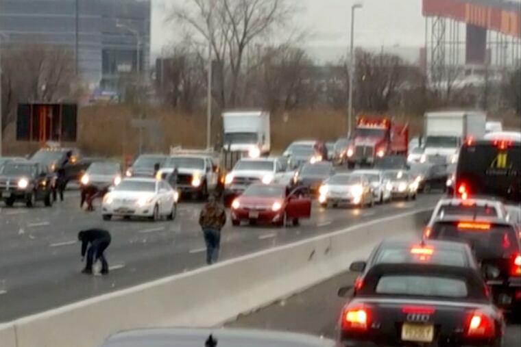 This screen shot from a video provided by Danielle Shah shows people picking up cash that spilled from an armored truck onto the highway in East Rutherford, N.J., near MetLife Stadium, Thursday, Dec. 13, 2018. Police say the incident caused multiple crashes as motorists stopped to grab the money from the truck that authorities say apparently had an issue with the locking device on one of its doors. (Danielle Shah/@dbholden417 via AP)
