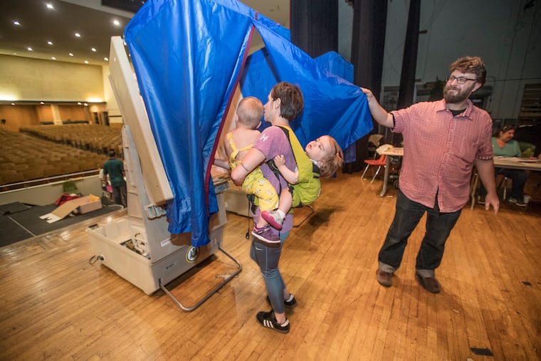 Vera Dugan, 18 months, right, holds on tight to Bridget Huffman, center, as she holds her son Drew Huffman, 20 months, left, as they all go into the voting booth together, on the stage of the auditorium of South Philadelphia High School on May 15, 2018. Nazim Karacaa, right, holds open the blue curtain so Huffman and her brood can enter to vote in the primary election in the 39th District in South Philadelphia.