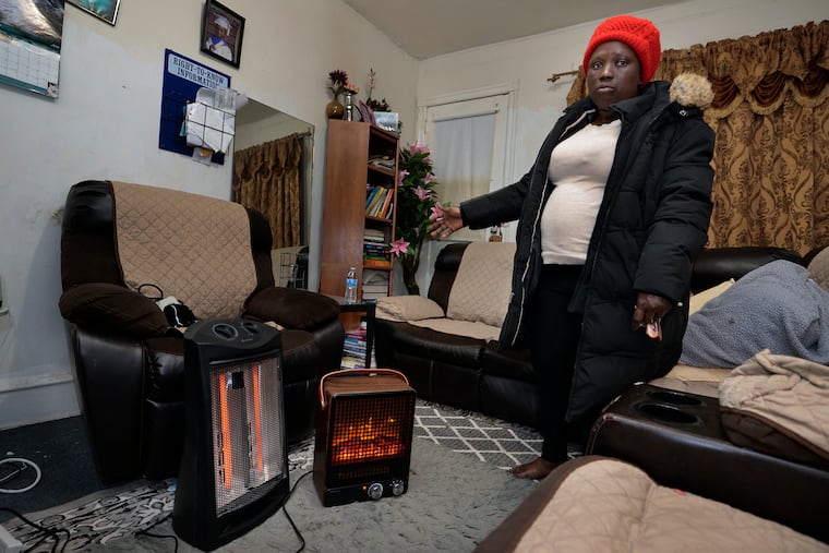 Wearing her winter coat and knit hat indoors, Ruth Stewart uses two space heaters to heat her living room in Kingsessing. Stewart, who lives in the apartment with her husband and three children, has not had any heat since a large water main break in her neighborhood last week.