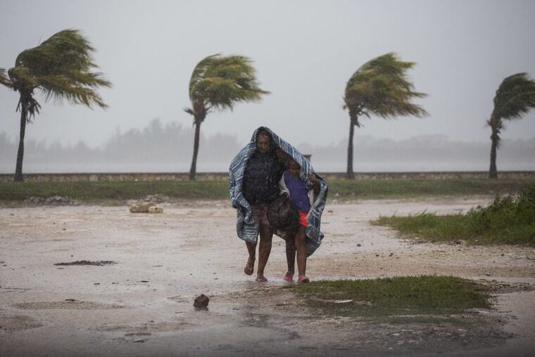 A woman and child use a blanket as protection from wind and rain as they walk in Caibarien, Cuba, on Friday.