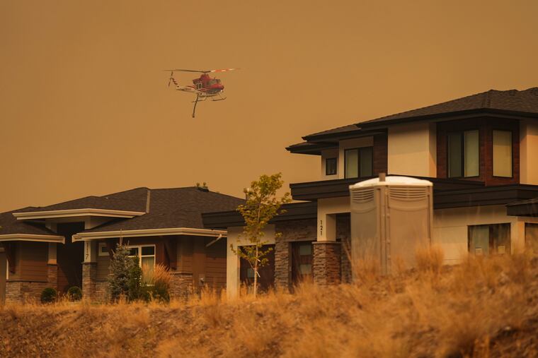 A helicopter equipped to respond to wildfires flies past homes in the Wilden neighborhood near Knox Mountain in West Kelowna, British Columbia, on Friday.