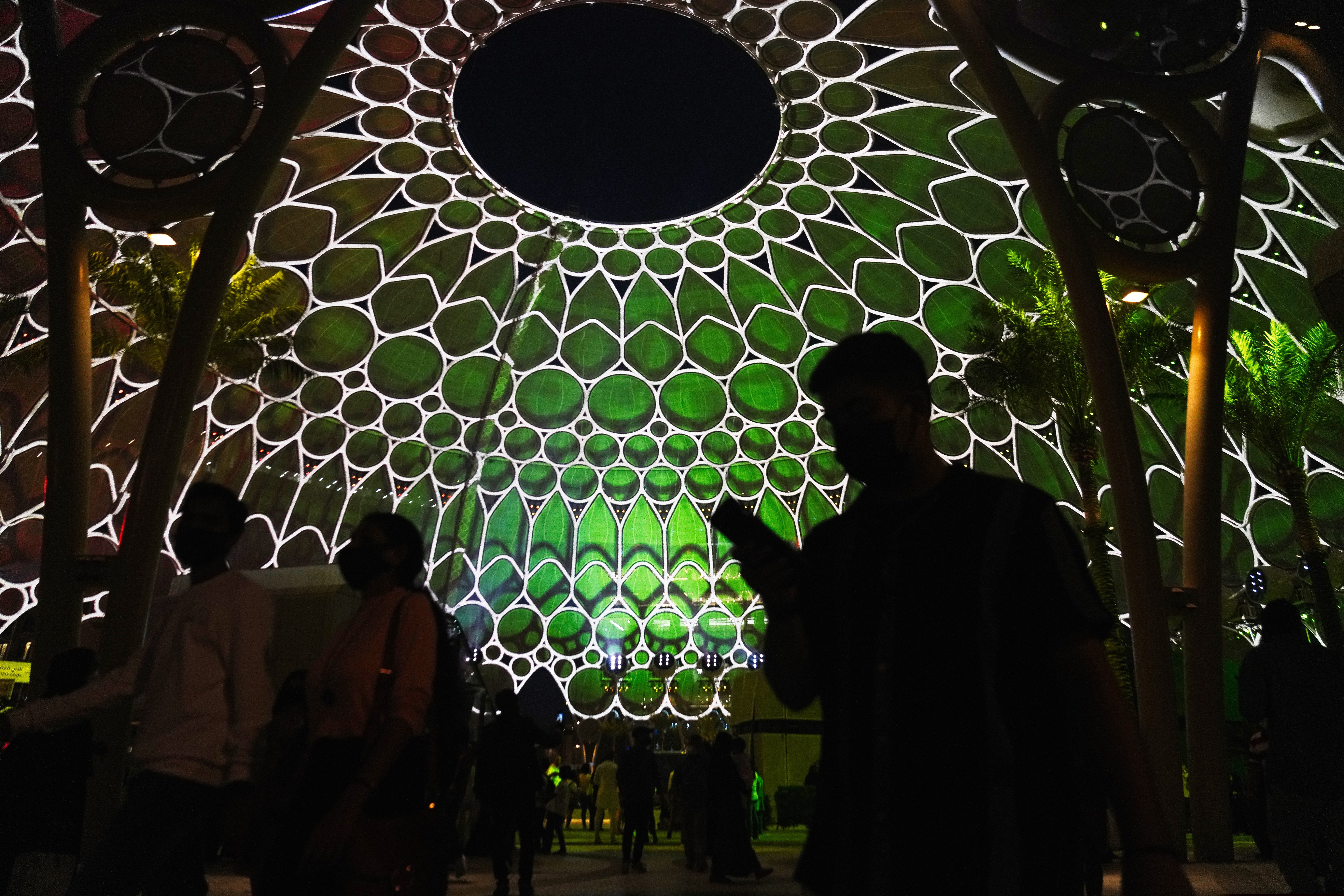People walk past the Al Wasl Dome as it is lit at night at Expo 2020 in Dubai, United Arab Emirates, Friday, Oct. 1, 2021. After eight years of planning and billions of dollars in spending, the Middle East's first ever World Fair opened on Friday in Dubai, with hopes the months-long extravaganza draws both visitors and global attention to this desert-turned-dreamscape.