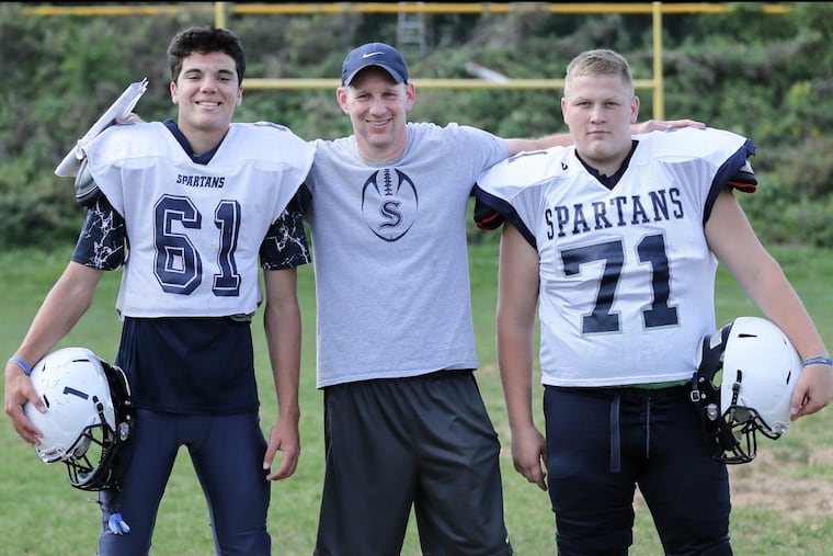 Springfield-Montco head football coach Chris Shelly is flanked by junior quarterback Max Perry (61) and senior two-way lineman Eddie Goldsmith. Due to a lack of numbers and experience, the Spartans played only one varsity game last season. STEVEN M. FALK / Staff Photographer
