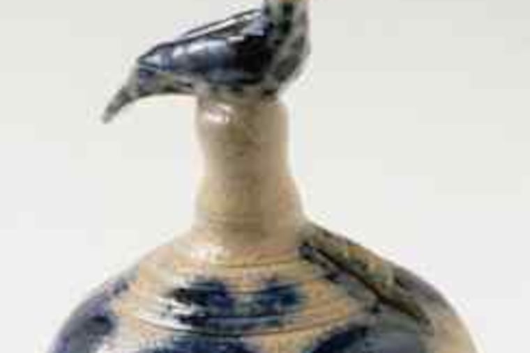 A coin bank attributed to Richard C. Remmey, 1880-90, featuring a hand-molded bird finial and a floral pattern in cobalt blue.
