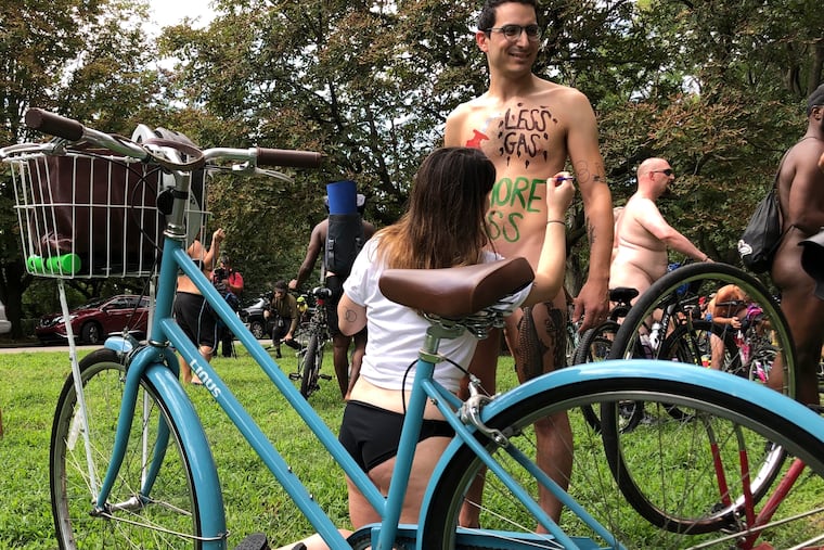 Nude bicyclist Oren Roth-Eisenberg has a message opposing fossil fuel consumption painted on his torso by his wife before the start of the Philly Naked Bike Ride in 2019.