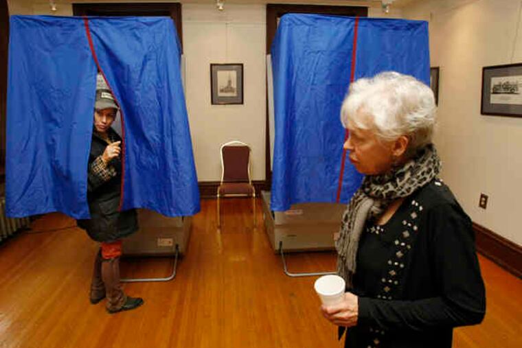 Elizabeth Sachs peeps out from a voting machine at the Media Borough Hall to ask a question, while Joye Asta, a machine inspector, keeps an eye on the equipment.
