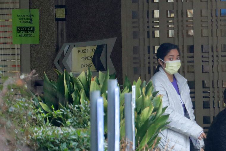 A person wearing a mask walks past a sign banning visitors at the Life Care Center in Kirkland, Wash., near Seattle on Monday. Dozens of people associated with the facility are reportedly ill with respiratory symptoms or hospitalized and are being tested for the COVID-19 virus.
