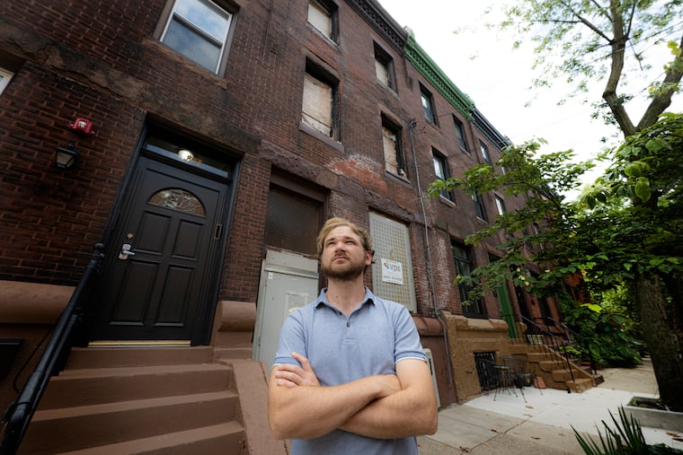 Eric Stone in front of a long-abandoned, boarded-up property near his home in Philadelphia. Residents of the 800 block of North 23rd Street say they've endured years of fly infestations, stormwater flooding, and wildlife taking shelter since the building burned down three years ago.