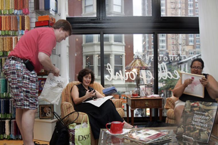 Russell Palmer, one of the owners of Rittenhouse Needlepoint, offers advice to Linda Webster as Yvette Jiggetts (right) stitches. (Bonnie Weller / Staff Photographer)