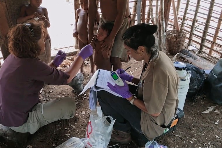 Rutgers scientist Maria Gloria Dominguez-Bello, left, uses cotton swabs to sample the microbiomes of children in the Amazon, as colleague Monica Contreras records their data.