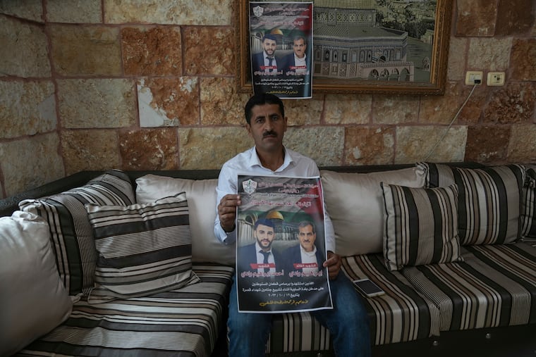 Abdelazim Wadi, 50, holds up a poster commemorating his brother, Ibrahim Wadi, and his nephew, Ahmed Wadi, who were killed by Israeli settlers during a funeral procession on Oct. 12 in the rural Palestinian village of Qusra, West Bank, on Sunday.