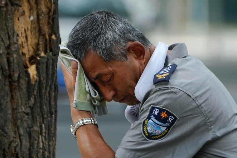 A security guard wearing an electric fan on his neck wipes away sweat on a hot day in Beijing on July 3, 2023.