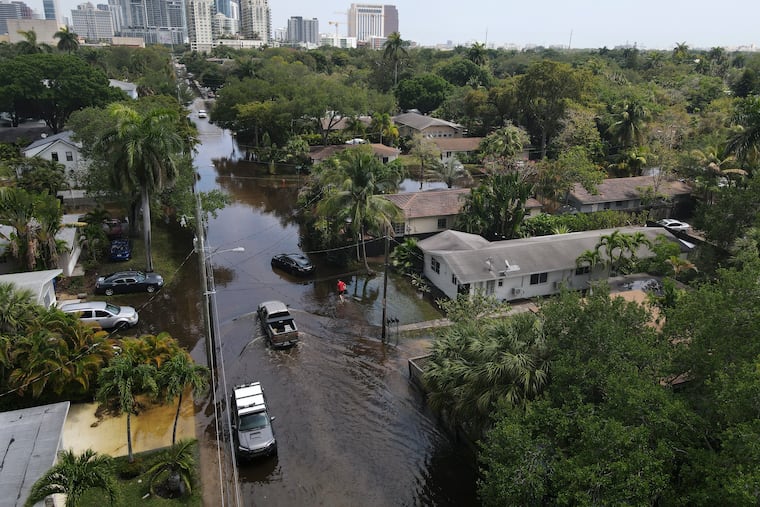 Trucks and a resident on foot make their way through receding floodwaters in the Sailboat Bend neighborhood of Fort Lauderdale, Fla., on Thursday.