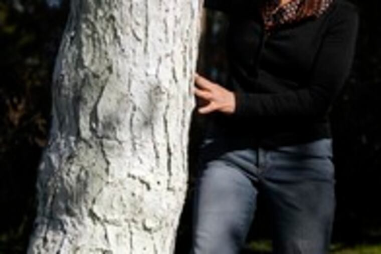 Patty Redenbaugh looks at the pine tree she painted white, cones and all, in her front yard. She chose white because it evoked fond memories of a birch she once had in Center City.