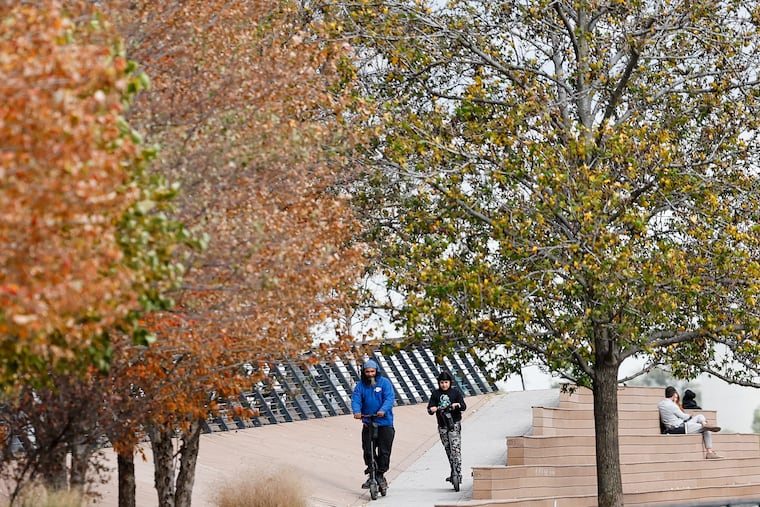 Electric scooter riders move near fall foliage at the Race Street Pier on Oct. 14, 2024. A $12 million federal grant to increase Philly's tree canopy has been unfrozen.