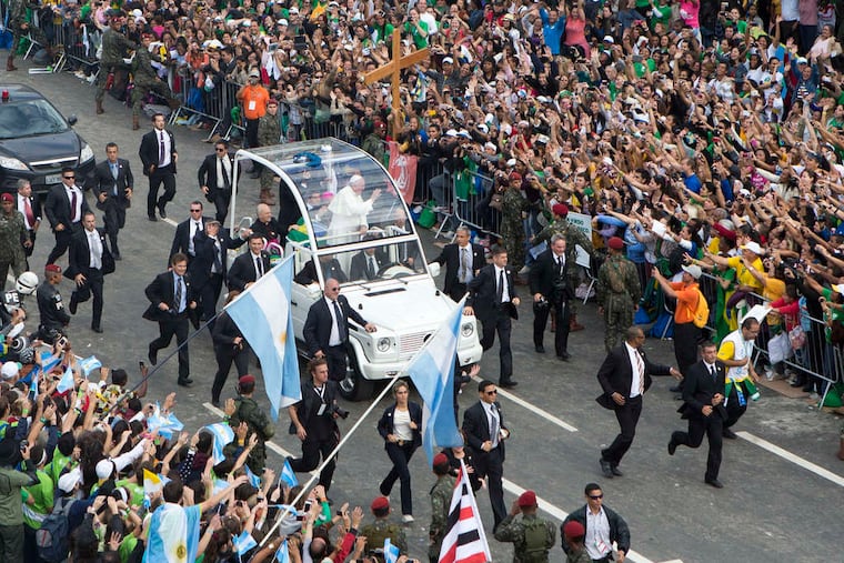 Surrounded by security, Pope Francis waves from the Popemobile during a visit to Rio de Janeiro in July 2013. His detail in Brazil wasleft frazzled by the pontiff's pushing his open-air vehicle so deep into the crowd that it was completely surrounded.