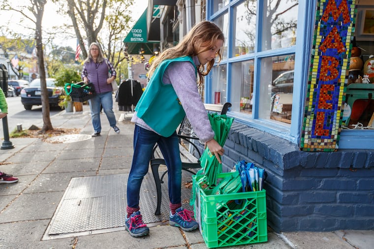 Maddie French, 10, restocks the reusable bags left in a milk carton in front of a business in Narberth,. The Montgomery County borough recently became the first municipality in Pennsylvania to pass an ordinance regulating single-use plastics, including bags and straws.