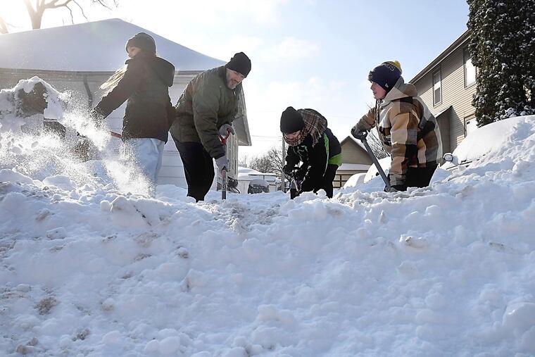 Nate LeBoutillier and his children, from left to right, Valerie, Gordie and Archie work to clear their neighbor's driveway Monday in North Mankato, Minn.