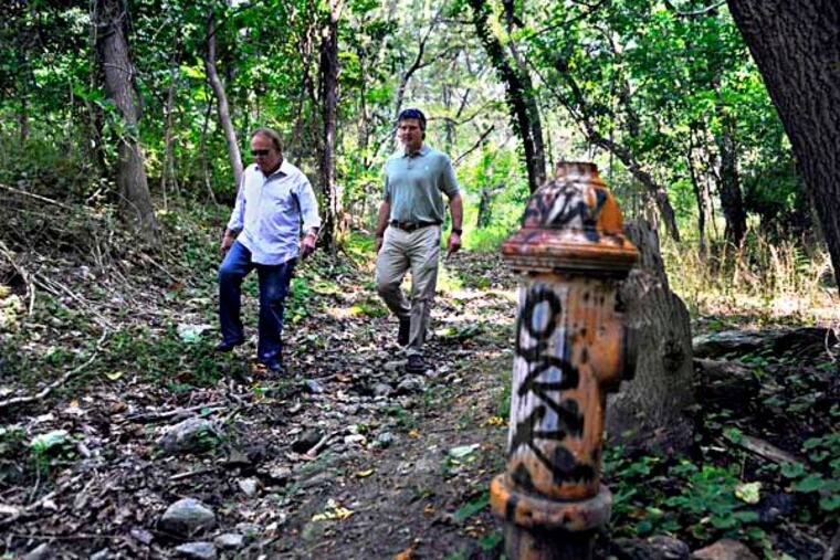 Greg Ventresca (right), with his attorney Anthony Twardowski (left), walks on the eight-acre portion of the hilly, wooded Germany Hill site he owns July 2, 2014. The fire hydrant, along with sewers, were installed, but a road was never built to the area which was zoned for residential use. The Ridge Park Civic Association opposed the plan for any development. ( TOM GRALISH / Staff Photographer )
