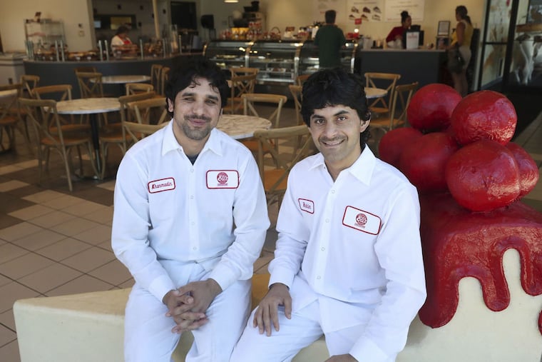 Khan Madin Ashna (left) and Rahimullah Zaland, former Afghan soldiers who fled their home country as the U.S. military withdrew last year, sit on a fiberglass cheesecake slice at Eli’s Cheesecake in the Dunning neighborhood of Chicago in August.