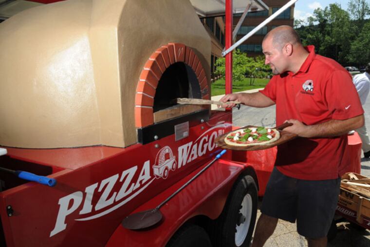 Josh Goldstein, 35, owner of Pizza Wagon lunch truck, slides a pizza
into his wood-burning pizza oven outside a King of Prussia office
complex June 20, 2013. Goldstein frequents office complexes, fairs,
festivals, little league games and any other venue where people like
to eat pizza. ( CLEM MURRAY / Staff Photographer )