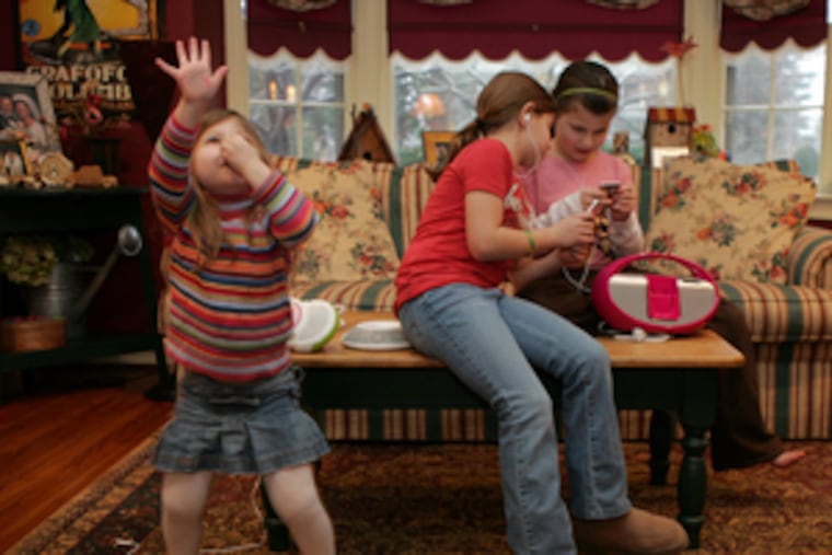 Maggie Waldman feels the beat and moves her feet to her digital music player. Older sisters Carly (center) and Sophie, illustrating the charm of earbuds, don't notice.