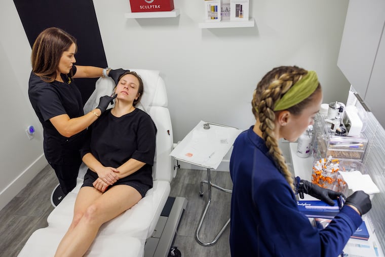 Aesthetic Nurse Practitioner Sarah Sidiqi prepares Julia O'Reilly for her fillers. O'Reilly lost 50 pounds on Ozempic and misses her fuller face. At right is medical assistant Courtney Brady.