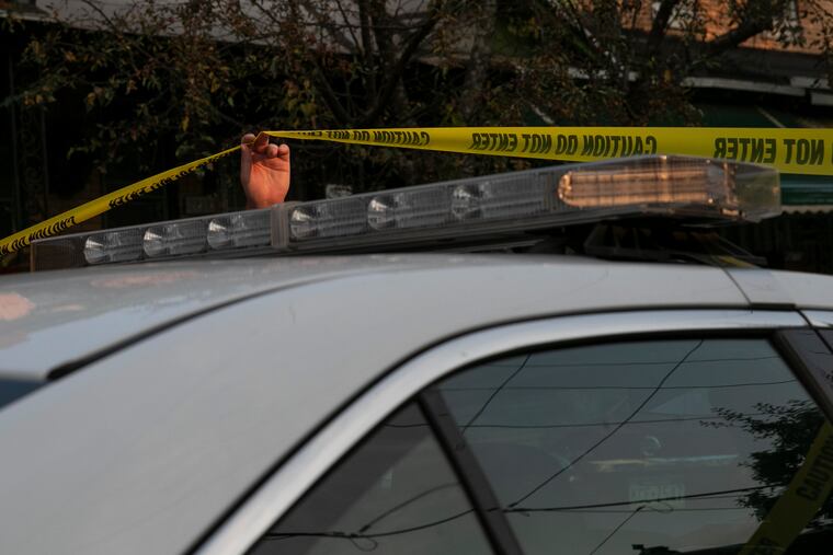 A police officer raises police tape to let a patrol car enter a scene in a file photograph.