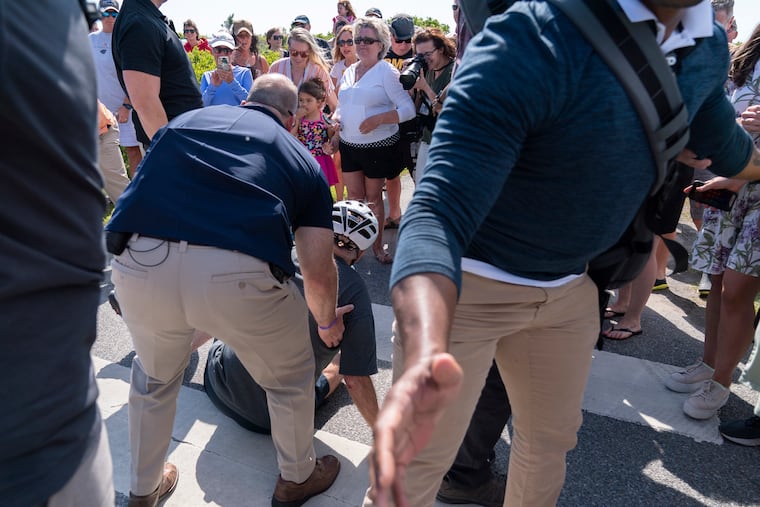 President Joe Biden is helped by U.S. Secret Service agents after he fell trying to get off his bike to greet a crowd on a trail at Gordons Pond in Rehoboth Beach, Del.