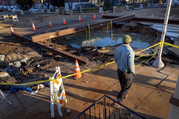 Ahmed Addy, a resident of Kingsessing neighborhood, walks past the large hole caused by the break in water line the day before.