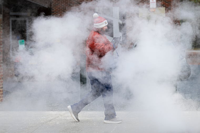 A pedestrian walks through a cloud of steam on a cold winter day in West Philadelphia, Friday, Dec. 26, 2025, as snow and a wintry mix are forecast for the area through Saturday morning.
