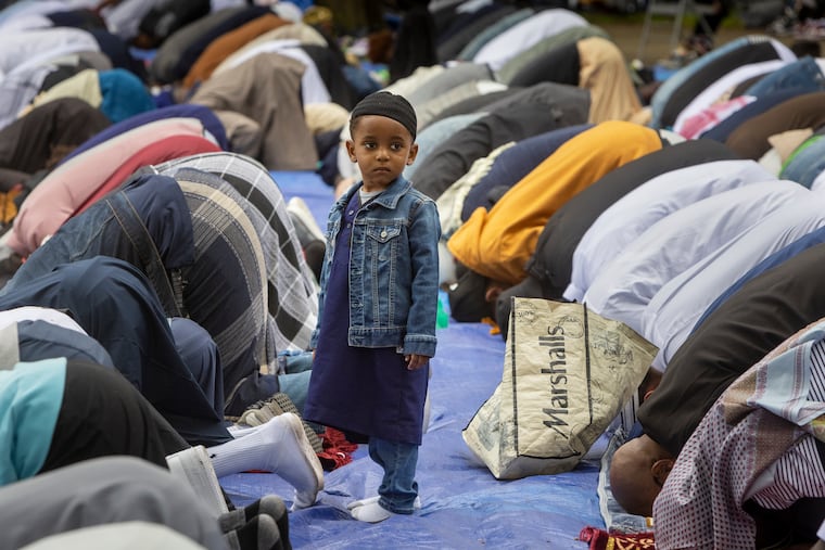 A young boy stands while all the men around him pray.