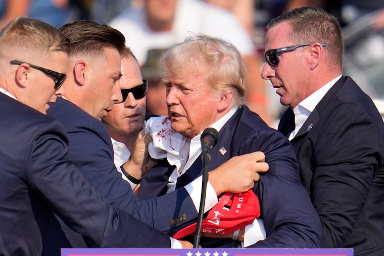 Former President Donald Trump is helped off stage by Secret Service agents following a shooting at his rally in Butler, Pa. Saturday.
