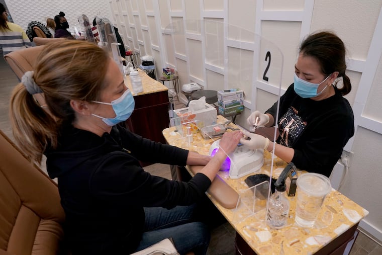 In this Jan. 25, 2021, file photo, Sara Nguyen, right, sits behind a plexiglass shield as she gives a manicure to Christine Frazer at KB Nails in Sacramento, Calif. (AP Photo/Rich Pedroncelli, File)