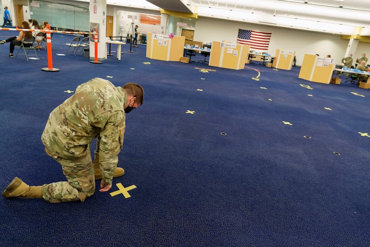Rhode Island Army National Guard Staff Sgt. Andrew Bates pulls up tape marking a line at a coronavirus mass-vaccination site at the former Citizens Bank headquarters in Cranston, R.I., June 10, 2021. Up to 40,000 Army National Guard soldiers across the country - or about 13% of the force — have not yet gotten the mandated COVID-19 vaccine, and as the deadline for shots looms, at least 14,000 of them have flatly refused and could be forced out of the service.