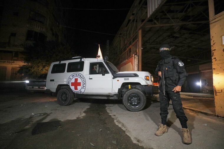 A gunman wearing the uniform of the al-Qassam Brigades, the military wing of Hamas, stands guard as Red Cross vehicles enter a warehouse in Gaza City allegedy to collect coffins containing the bodies of four deceased hostages.