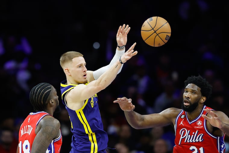 Golden State Warriors guard Donte DiVincenzo passes the basketball between Sixers center Joel Embiid and guard Shake Milton during the second quarter. DiVincenzo played collegiately at Villanova.