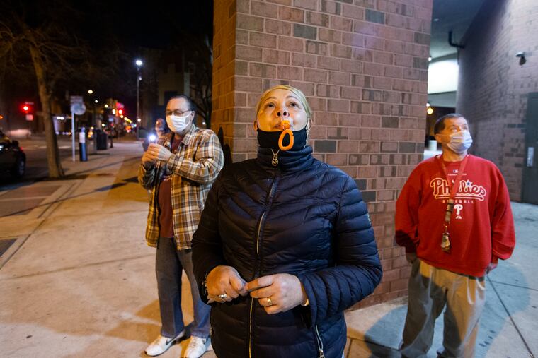 (Left to right) George Bunting, Victoria Gonzales, and Will Houlne on Wednesday night outside the American Postal Workers Housing Complex at Eighth and Locust Streets. Each night at 7 p.m. for the past year that COVID-19 has shut down so much of Philadelphia, they have gathered with another friend, Fred Kirby, to blow whistles and bang a pan in tribute to health-care workers at nearby Pennsylvania and Thomas Jefferson University Hospitals.