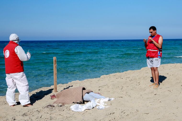 Libyan Red Crescent workers stand around a body of a drowned migrant near the city of Khoms, some 60 miles east of Tripoli, Libya, on Friday, July 26, 2019. Libya's coast guard recovered dozens of bodies of Europe-bound migrants who perished at sea as search operations continued Friday, a day after up to 150 people, including women and children, went missing and were feared drowned after their boats capsized in the Mediterranean Sea.