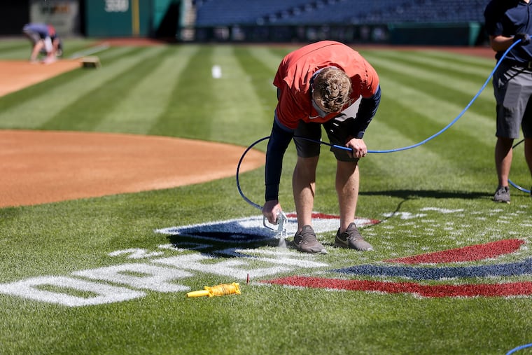 Jeremy Wilt, manager of field operations, paints the “Opening Day” logo on the field at Citizens Bank Park. Phillies manager Joe Girardi is thrilled that fans will be back in the ballpark for the 2021 opener and season.