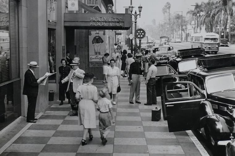 Hollywood Roosevelt Hotel Bellhop Richard Brian, center in dark shirt and cap, talks with a bus driver amid a busy street scene in the 1940s. Note the palm trees in the background and the man at left, preparing to greet the man reading a newspaper.