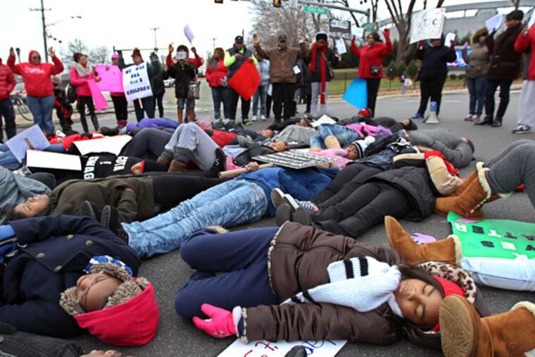 Brianna Clark, 8, center, and dozens of other children lie down on City Avenue and Monument Road to hold their die-in protest, as their parents stand around them in a circle with their hands up in a "don't shoot" pose Saturday. ( Michael Bryant / Staff Photographer )